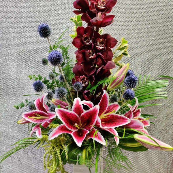 Tall floral arrangement with pink lilies, burgundy orchids, and blue thistle in a vase