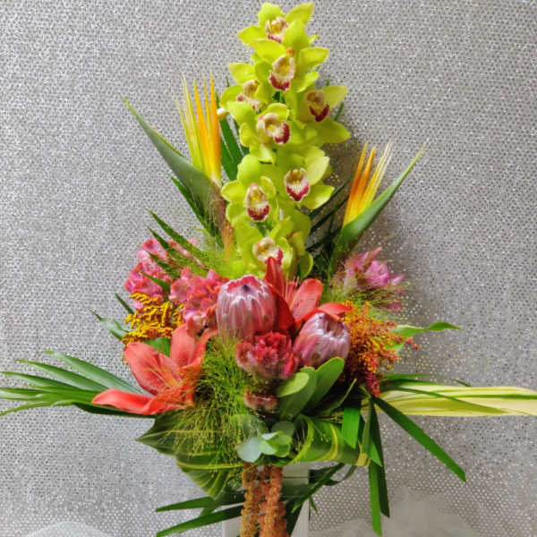 Tall tropical bouquet with green orchids and pink protea in a white vase