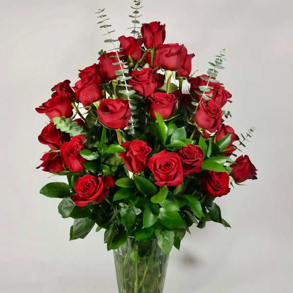 Red roses arranged in a clear glass vase with eucalyptus accents