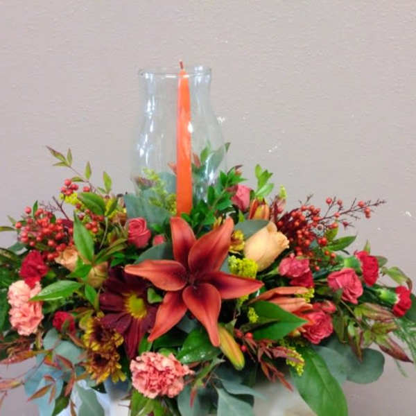 Mixed floral arrangement in a clear glass vase with an orange candle