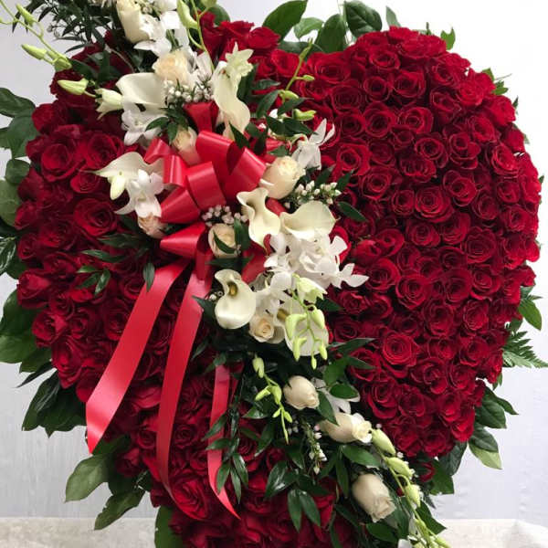 Heart-shaped red rose arrangement with white flowers and a red ribbon