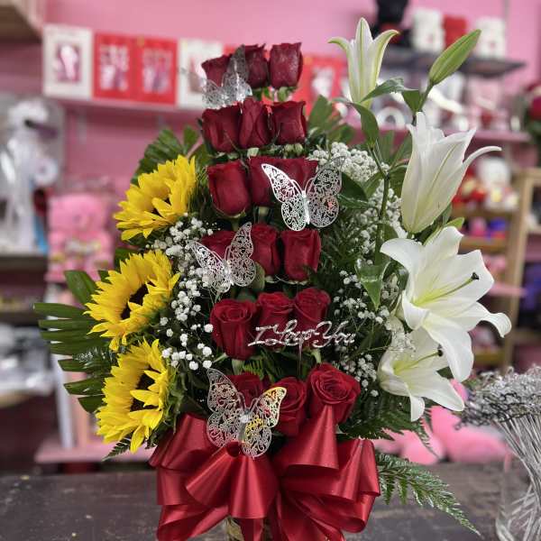 Tall basket arrangement of red roses, white lilies, yellow sunflowers, and silver butterflies with a red ribbon bow.