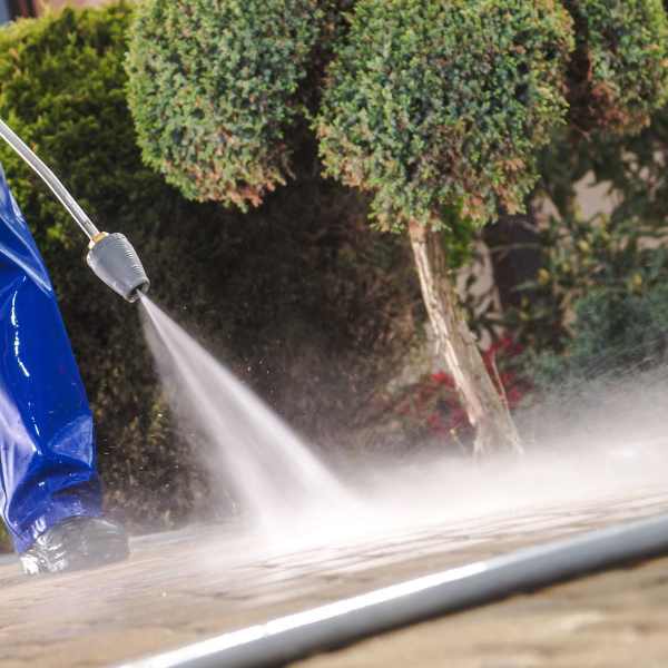 Person in blue protective pants pressure-washing a paved surface outdoors