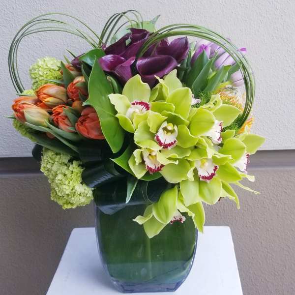 Mixed bouquet with green orchids, purple calla lilies, and orange tulips in a glass vase
