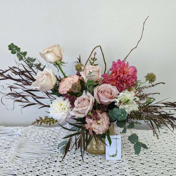 Blush and white floral arrangement in a gold vase with long burgundy foliage