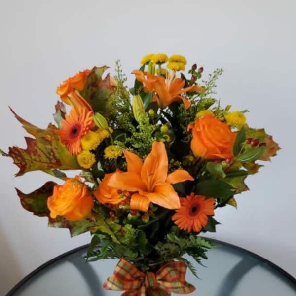 Orange lilies and roses in a glass vase with a plaid bow