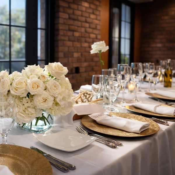 White floral centerpiece on a set dining table with glassware and gold chargers