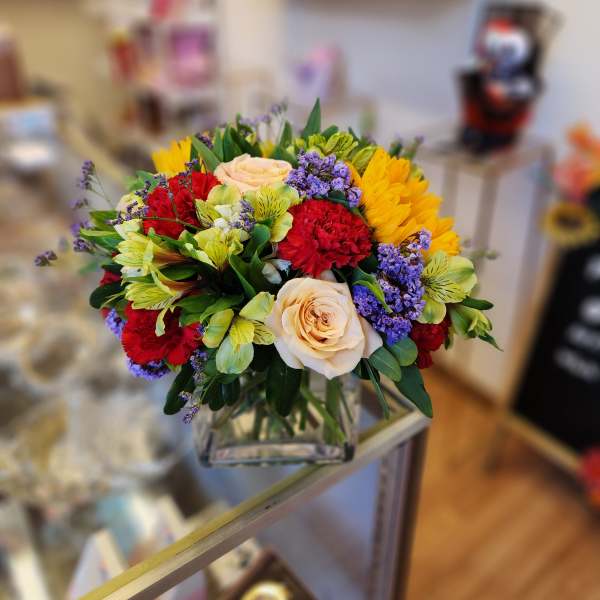 Mixed bouquet of roses, carnations, and purple filler in a glass vase