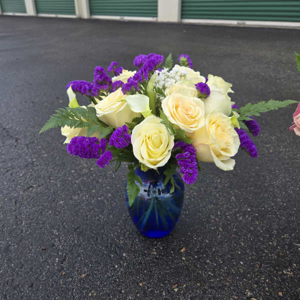 Bouquet of pale yellow roses and purple filler flowers in a blue glass vase