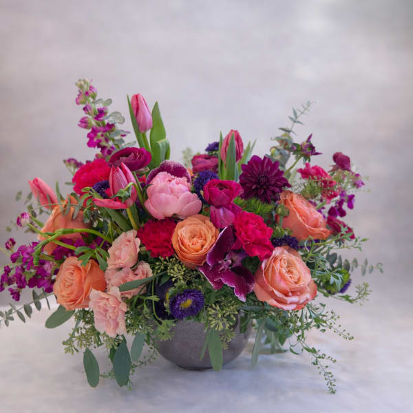 Mixed pink, peach, and purple flowers arranged in a gray bowl