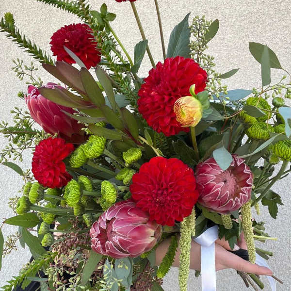 Bouquet of red and pink flowers with greenery and a white ribbon