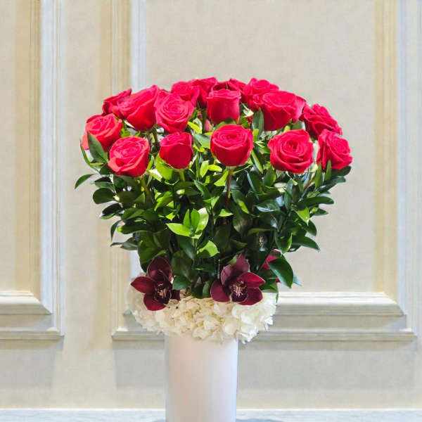 Red roses arranged in a white vase with white and burgundy flowers