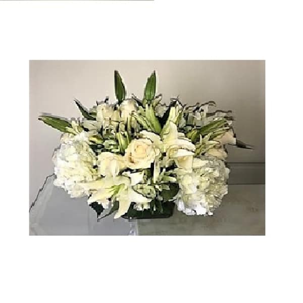 Low white arrangement of roses, lilies, and hydrangeas in a rectangular glass vase