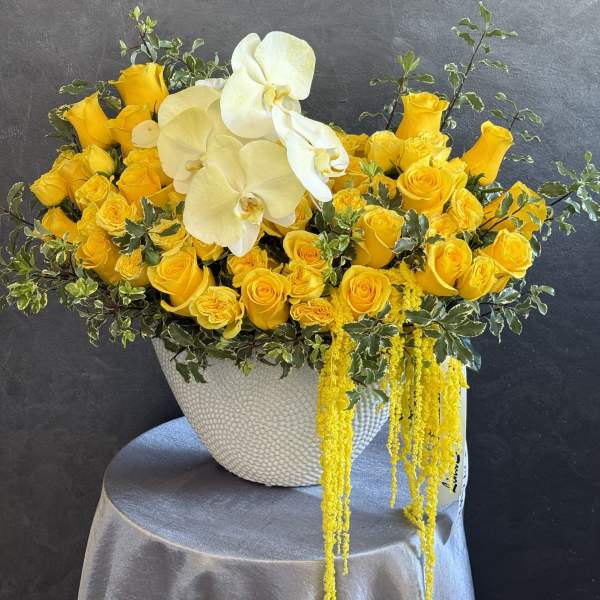 Yellow roses and white orchids in a textured white vase