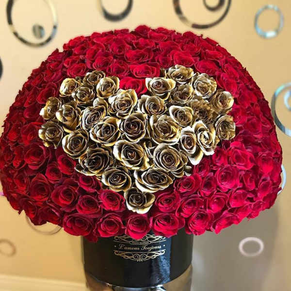 Large dome of red roses with a gold rose heart in a black hatbox on a tall pedestal.