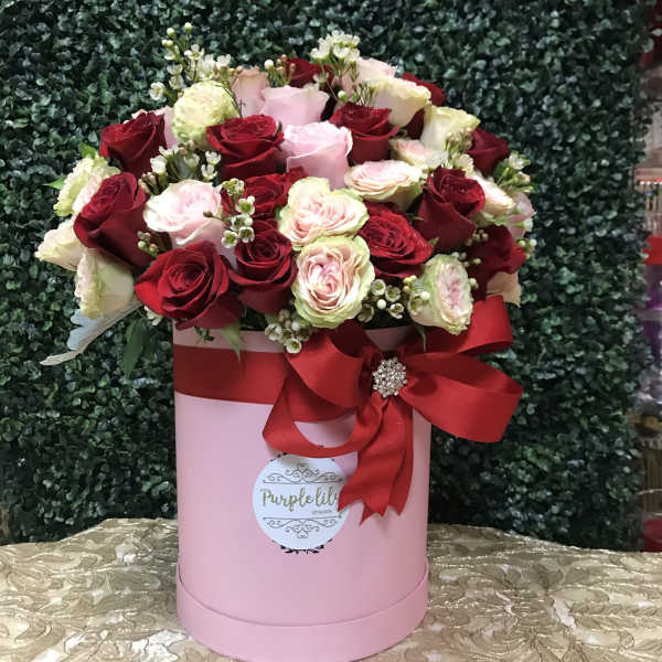Pink hatbox arrangement of red and blush roses with a red ribbon