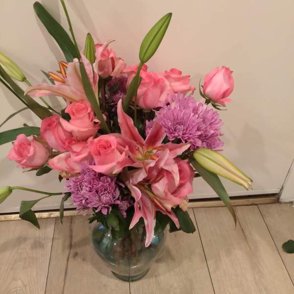 Pink roses and lilies in a glass vase with purple mums