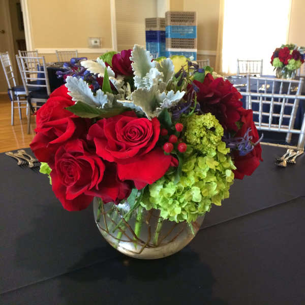 Red roses and green hydrangeas in a glass bowl vase on a table