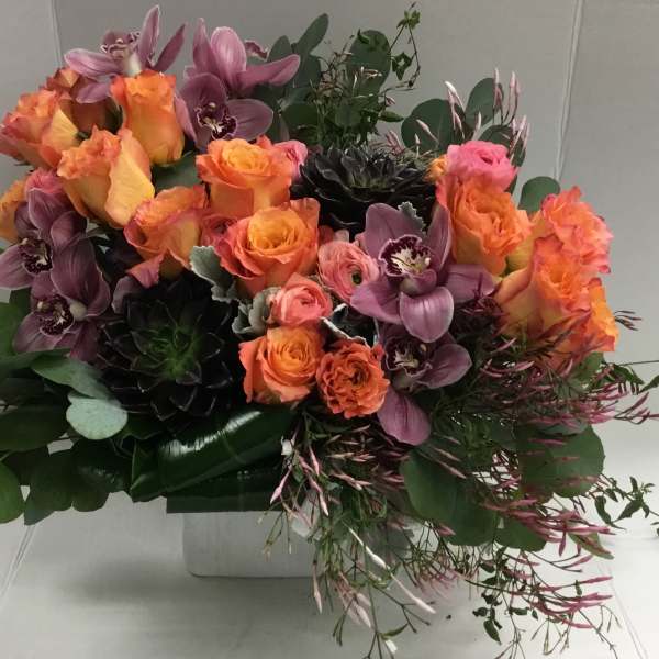 Bouquet of orange roses and purple orchids in a white container