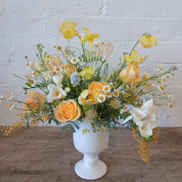 Yellow and peach floral arrangement in a white pedestal vase