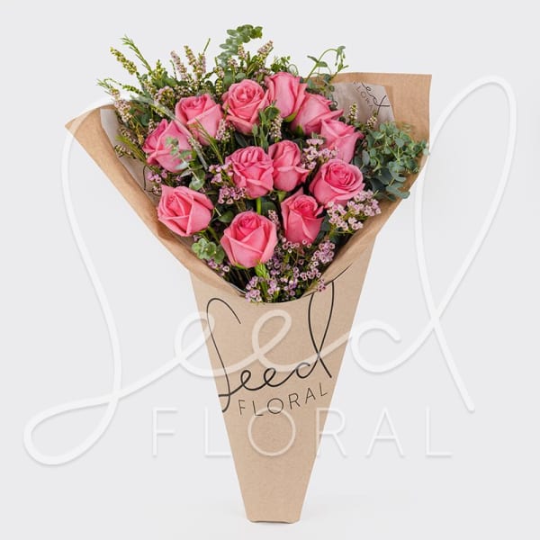 Cone-wrapped bouquet of pink roses with small pink filler flowers in kraft paper