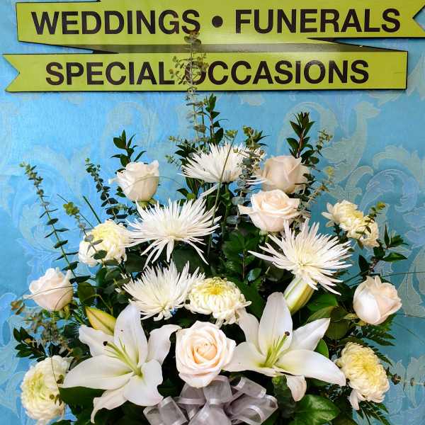 White floral arrangement in a woven basket with a silver ribbon
