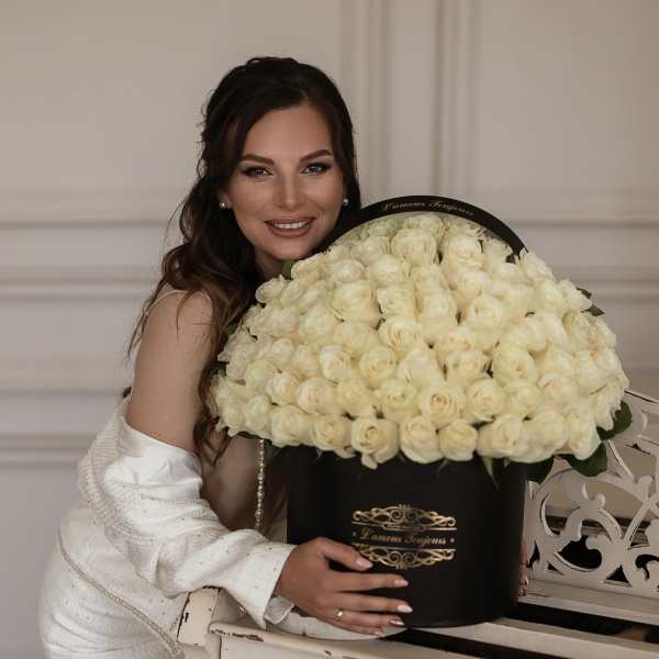 Large black hatbox filled with cream roses beside a smiling woman in white.
