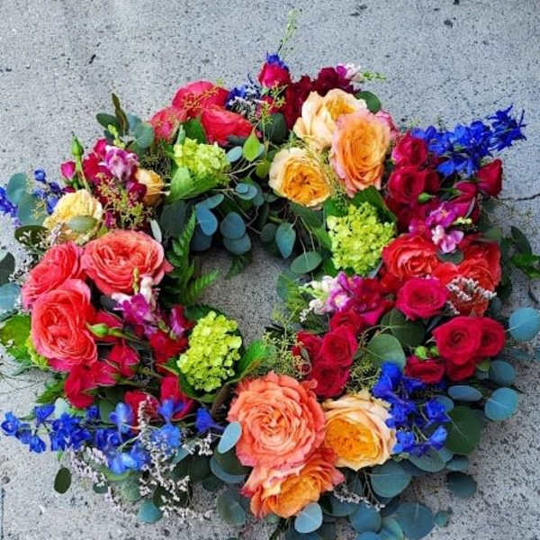 Bright circular wreath of roses, hydrangea, and blue delphinium on a concrete surface