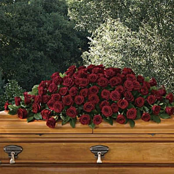 Large spray of dark red roses arranged on top of a wooden casket outdoors