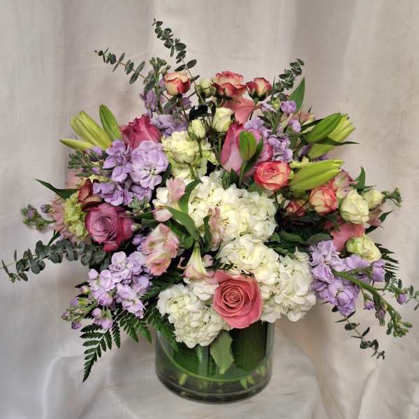 Large mixed arrangement of pink roses, white hydrangeas, lavender blooms and lilies in a clear glass vase