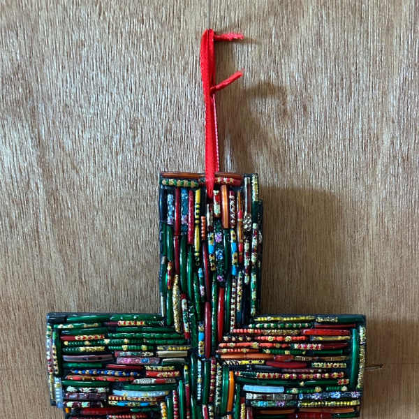 Colorful beaded mosaic cross ornament with a red hanging ribbon on a wood surface