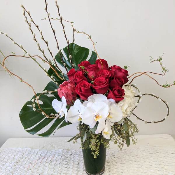 Red roses and white orchids in a tall vase with large leaves