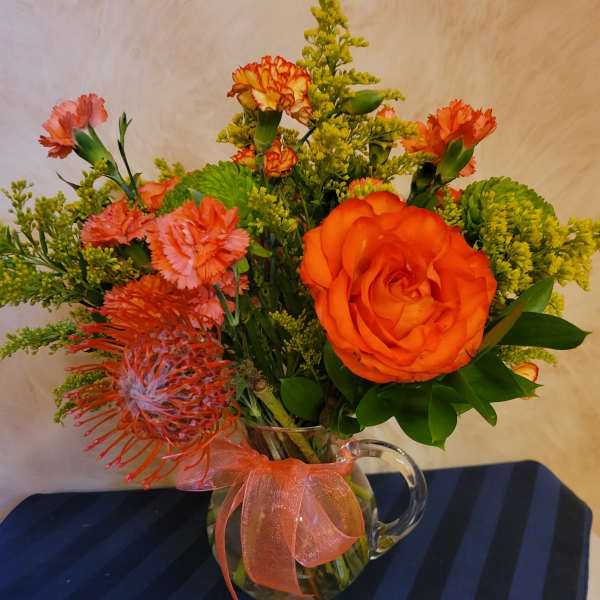 Orange and pink mixed bouquet in a glass pitcher vase with ribbon