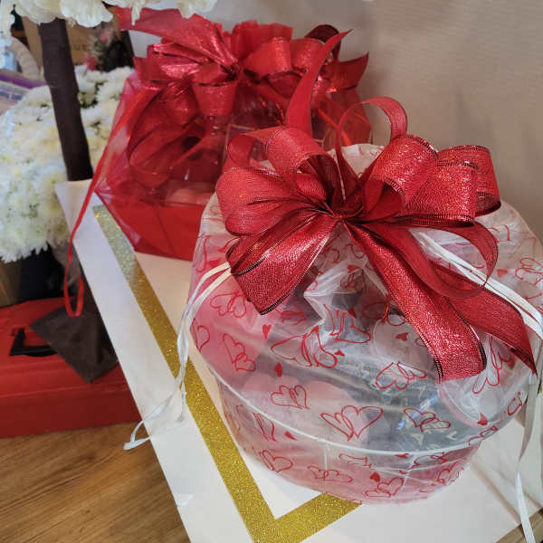 Gift baskets wrapped in heart-patterned cellophane with red bows and white flowers above