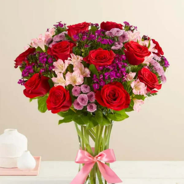Bouquet of red roses and pink flowers in a clear glass vase with a pink ribbon