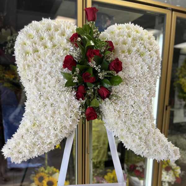 Standing angel wing tribute of white chrysanthemums with red roses on an easel