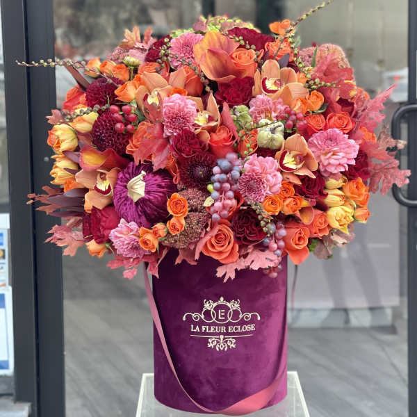 Large bouquet of orange, pink, and red flowers in a purple hatbox
