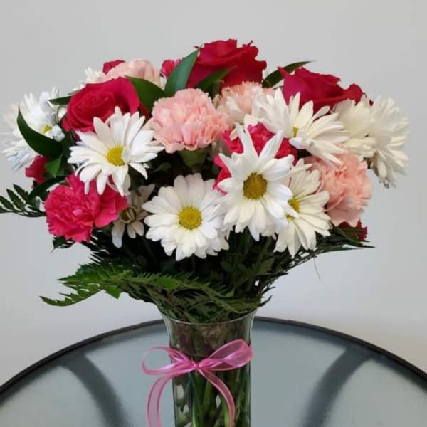 Bouquet of red roses, pink carnations, and white daisies in a glass vase