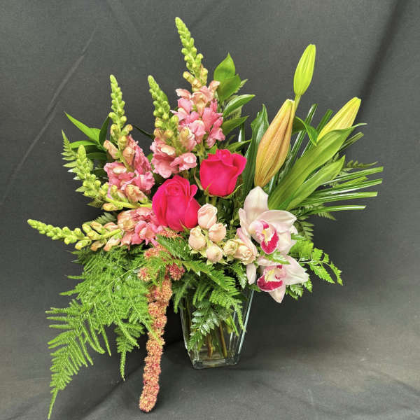 Pink roses and orchids in a clear glass vase with tall greenery