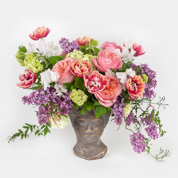 Pink and purple flower arrangement in a sculpted face vase