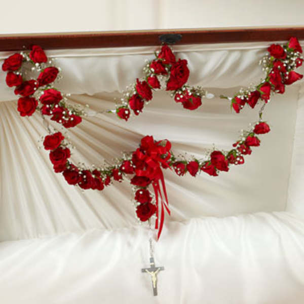 Red rose garlands with bow and rosary cross draped inside a white lined casket lid