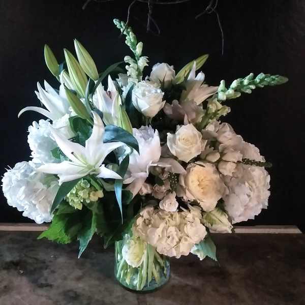 White floral arrangement with lilies, roses, and hydrangeas in a glass vase