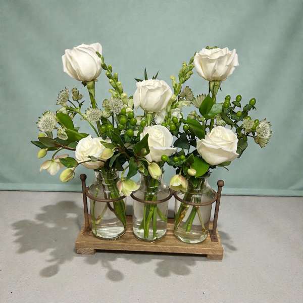 White roses arranged in three glass jars on a wooden holder