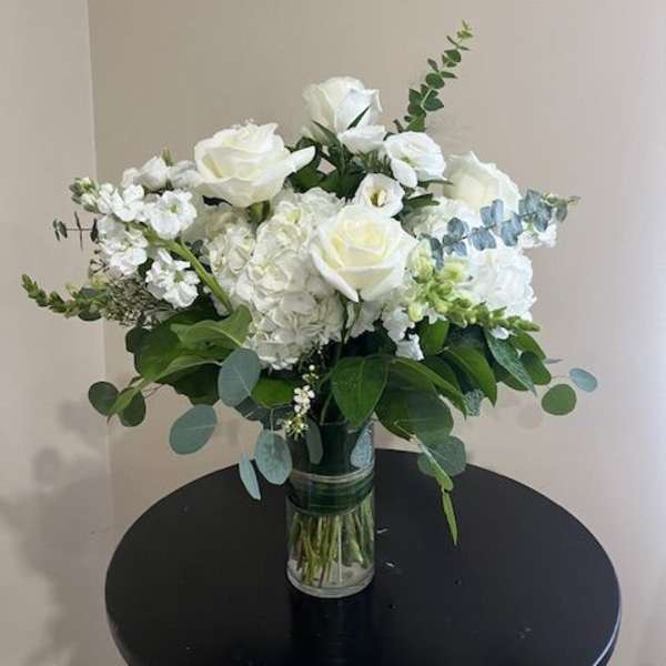 White roses and hydrangeas with eucalyptus in a clear glass vase on a round black table