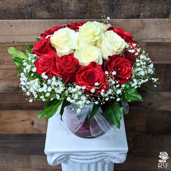 Red and white roses arranged in a glass vase with baby's breath