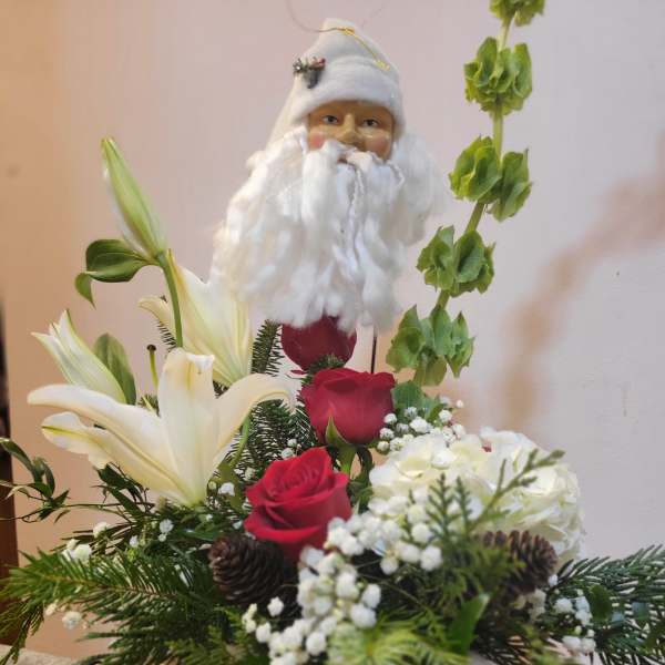 Santa figurine holding a floral arrangement with red roses and white lilies