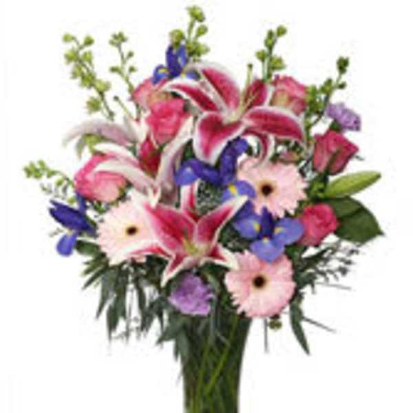 Mixed bouquet of pink lilies, gerbera daisies, and purple flowers in a glass vase