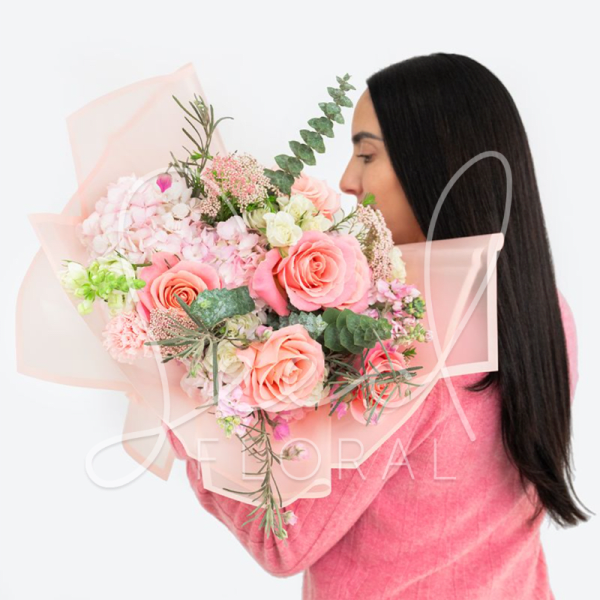 Woman holding a pink and peach bouquet with roses and hydrangeas
