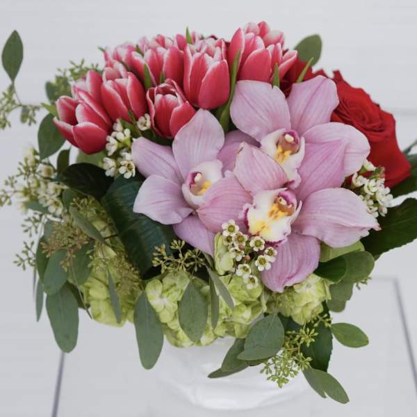 Bouquet of pink tulips, orchids, and red roses in a white vase