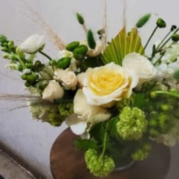 White and green floral arrangement with a yellow-centered rose in a vase